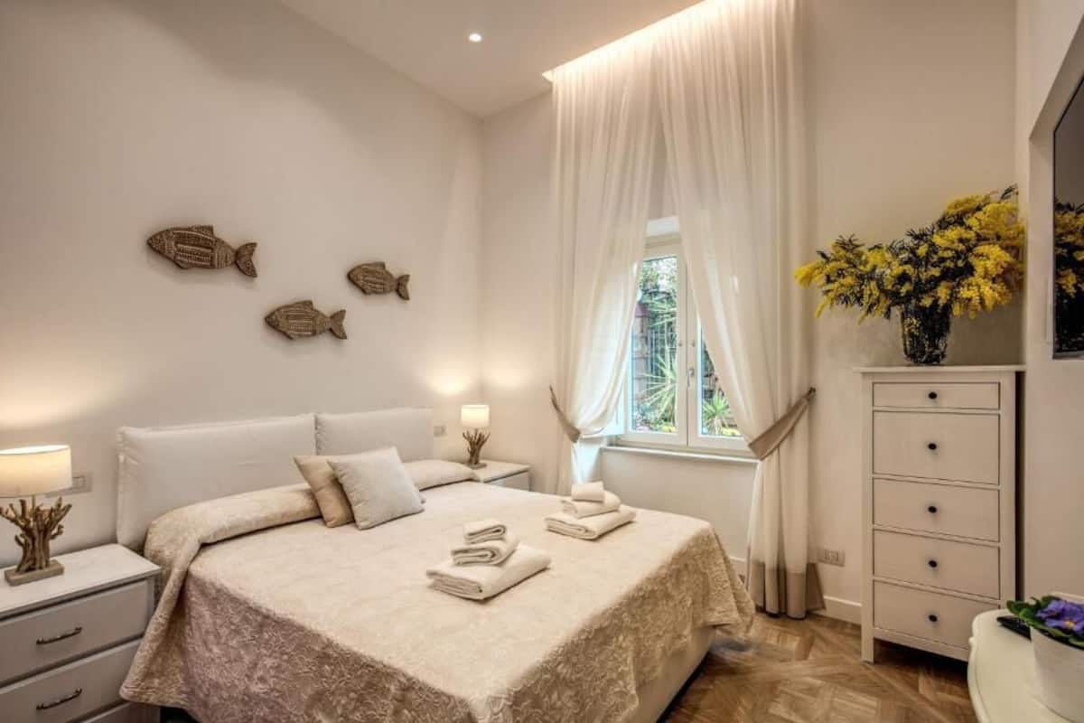 A bedroom with a bed, nightstands, a dresser, and a window with curtains.