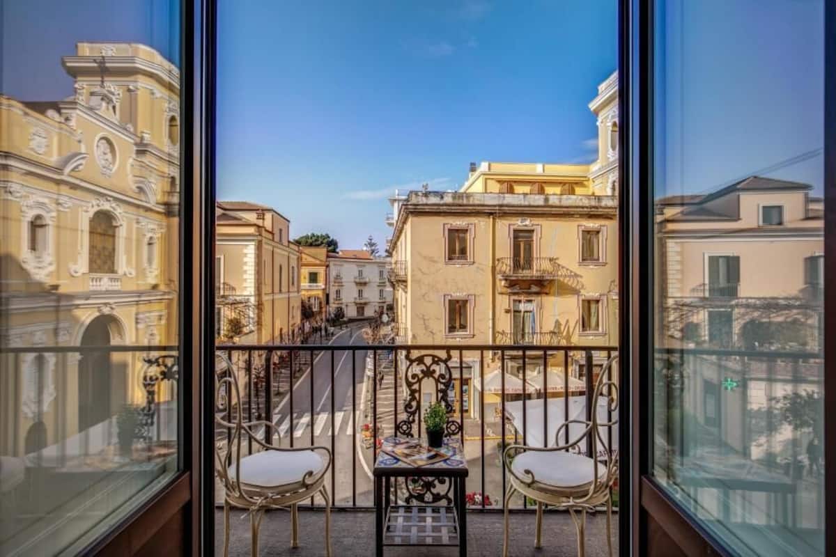 A balcony with two chairs and a small table, overlooking a street with historic buildings.