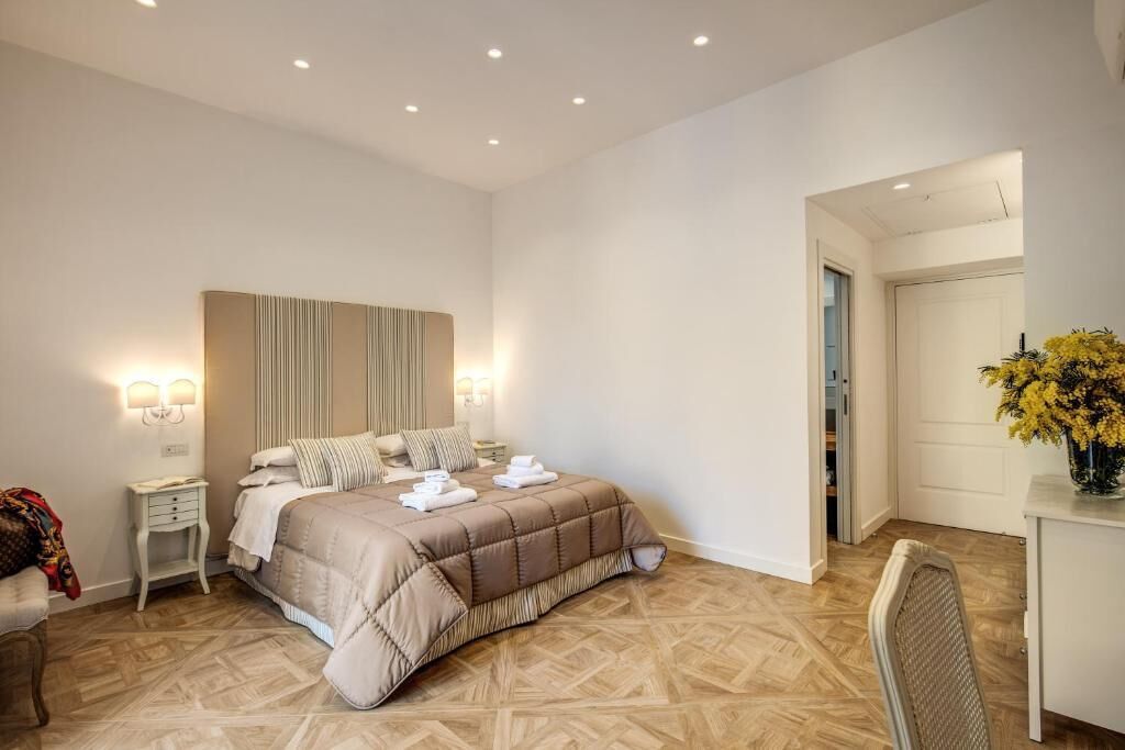 A bedroom with a large bed, bedside tables, a chair, and a desk with a vase of flowers.