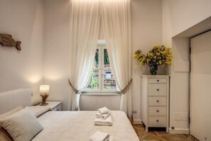 A bedroom with a bed, a nightstand, a dresser, and a window with curtains. - Sorrento Square Suites (Sorrento)