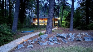 A lodge surrounded by tall trees, with a pathway leading to the entrance. - 💥New💥Sandy Beach! Main lake, kayaks, dock, hot tub, theater, game room, dogs! (Henrico)