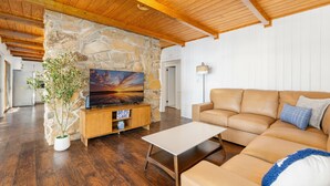 A living room with a stone wall, wooden ceiling, a flat-screen TV, a sofa, and a coffee table. - 💥New💥Sandy Beach! Main lake, kayaks, dock, hot tub, theater, game room, dogs! (Henrico)