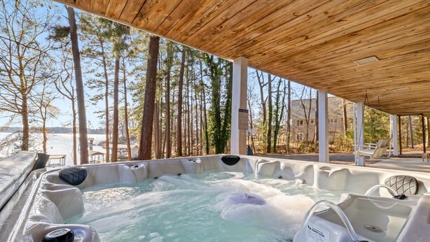 A hot tub area with a wooden ceiling, surrounded by trees and a view of a beach. - 💥New💥Sandy Beach! Main lake, kayaks, dock, hot tub, theater, game room, dogs! (Henrico)