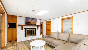 A living room with a fireplace, a sofa, a coffee table, and wooden cabinets. - 💥New💥Sandy Beach! Main lake, kayaks, dock, hot tub, theater, game room, dogs! (Henrico)
