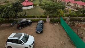 A view of a resort with multiple buildings, a dirt parking area, and a hilly landscape in the background. - Vanantara Courtyard (Alwar)