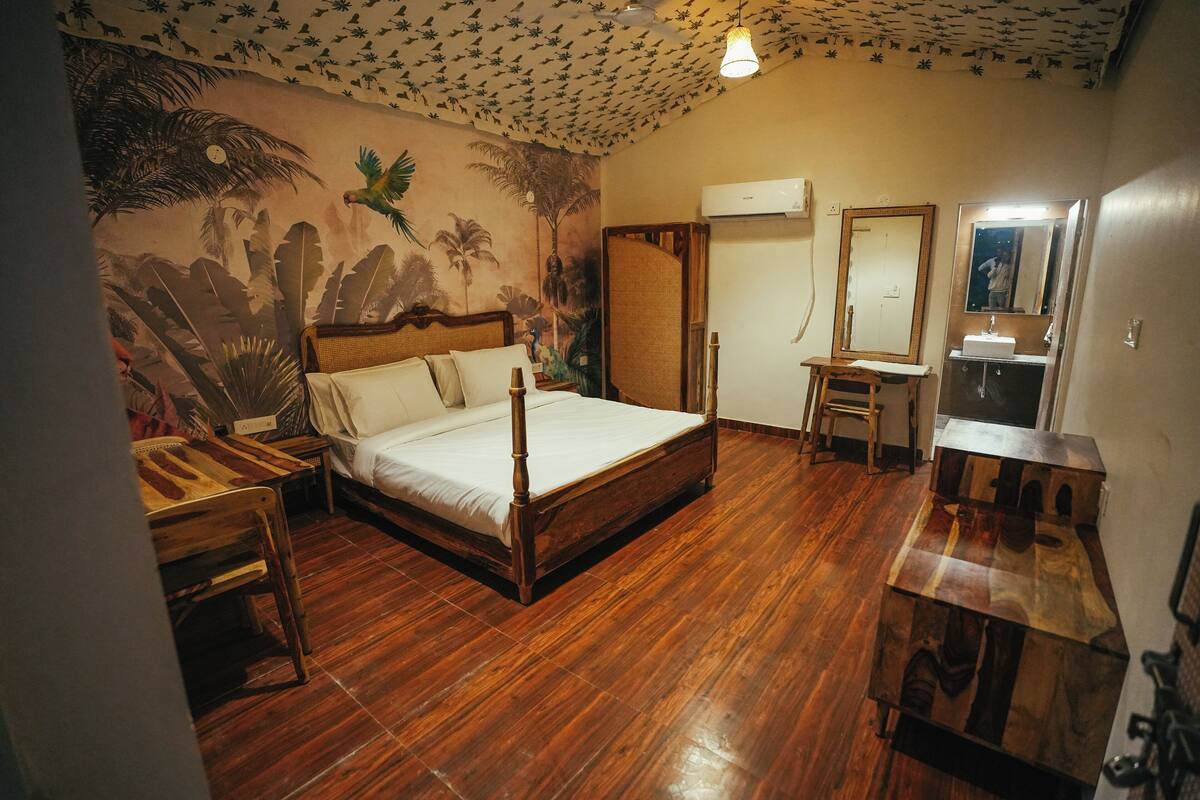 Una habitación con cama, un escritorio de madera, un espejo y un baño con lavamanos y espejo.