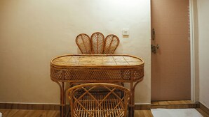 A room with a round table and two wicker chairs, a ceiling with a pattern of palm trees and elephants, a light fixture, and a door with a mesh screen. - Vanantara Courtyard (Alwar)