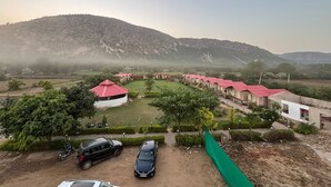 A rural setting with a row of red-roofed cottages, a dirt road, and a hilly landscape in the background. - Vanantara Courtyard (Alwar)