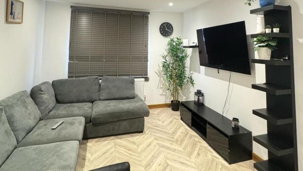 Uma sala de estar moderna com um sofá modular, uma televisão de tela plana, um vaso de planta e um piso com padrão herringbone.