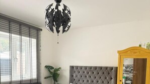 Quarto com cabeceira estofada, cama grande com roupa de cama branca, tapete listrado azul escuro e dourado, armário de madeira com espelho e planta em vaso.