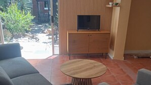 Una sala de estar con un televisor sobre un mueble de madera, una mesa redonda de madera y sofás grises.