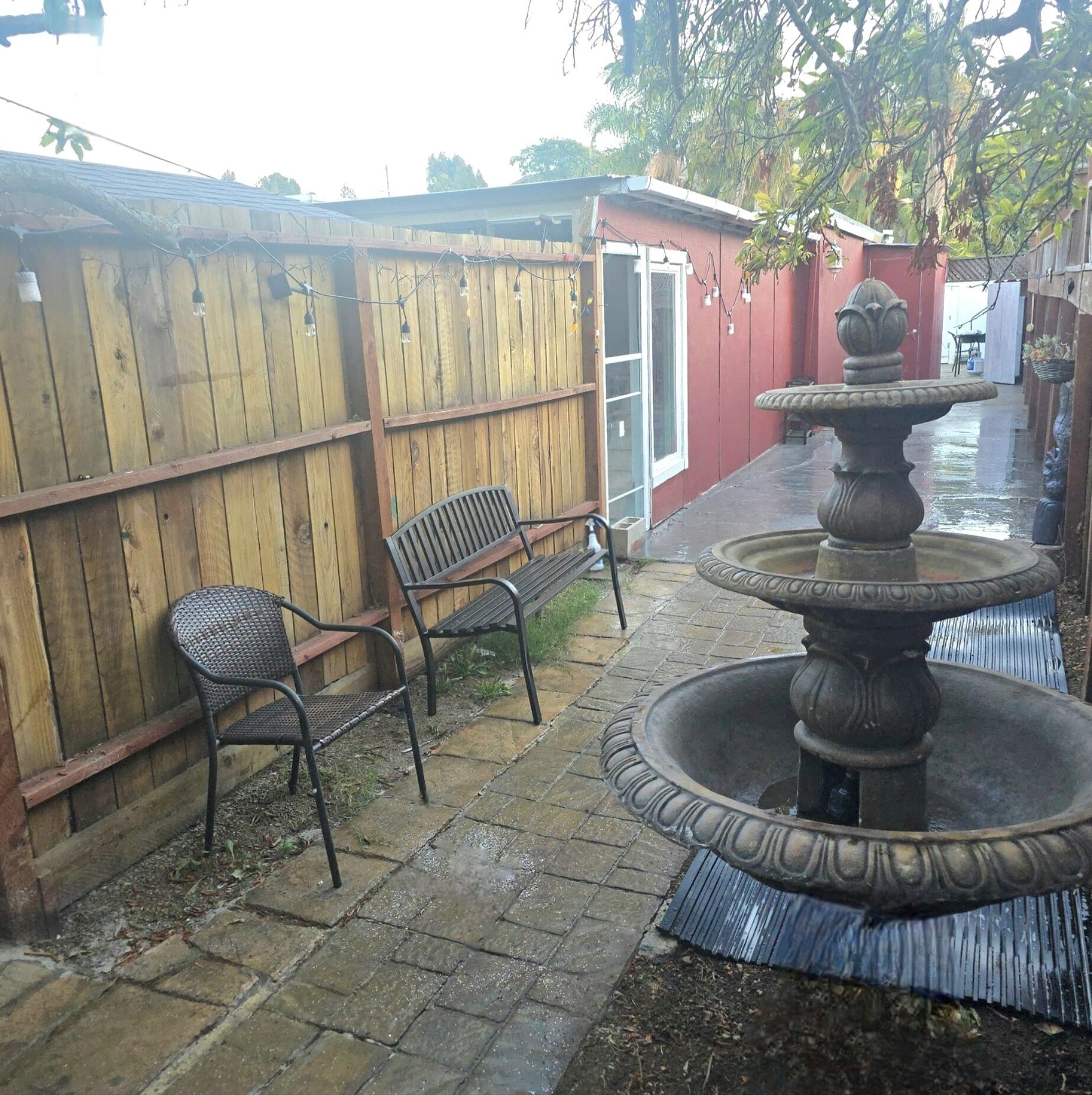 A patio with a wooden fence, two metal chairs, and a stone fountain.