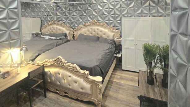 Ein Schlafzimmer mit einer gesteppten Kopfteil, einem Nachttisch mit Lampe, einem Kleiderschrank und einem Blumentopf.