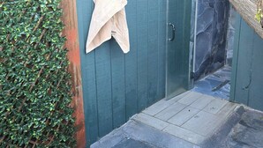 Ein Wellnessbereich mit Holzlattengitterwand, einem Handtuch an einem Haken, einer Glastür und einem Steinboden.