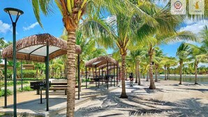 Una zona sulla spiaggia con costruzioni a tetto di paglia, palme e cielo sereno.