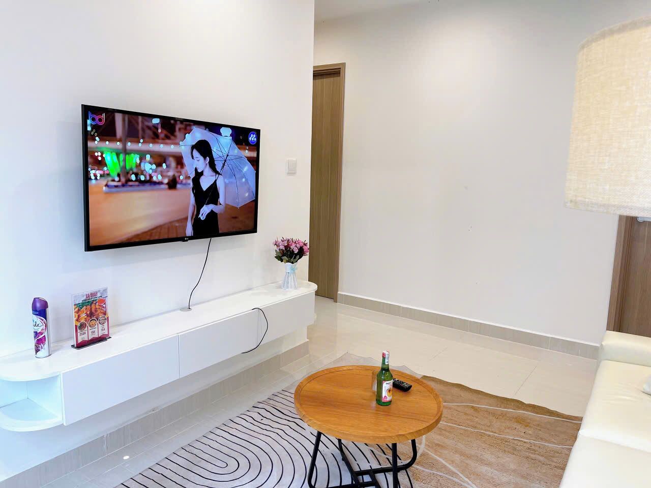 Un salon moderne avec un téléviseur à écran plat fixé au mur, un meuble de rangement blanc en dessous, une table basse ronde en bois et un tapis à motifs.