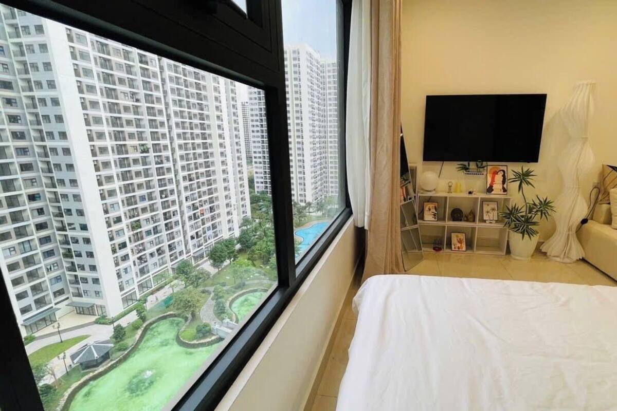 A hotel room with a large window, a bed, a TV, a small table, and a couch.