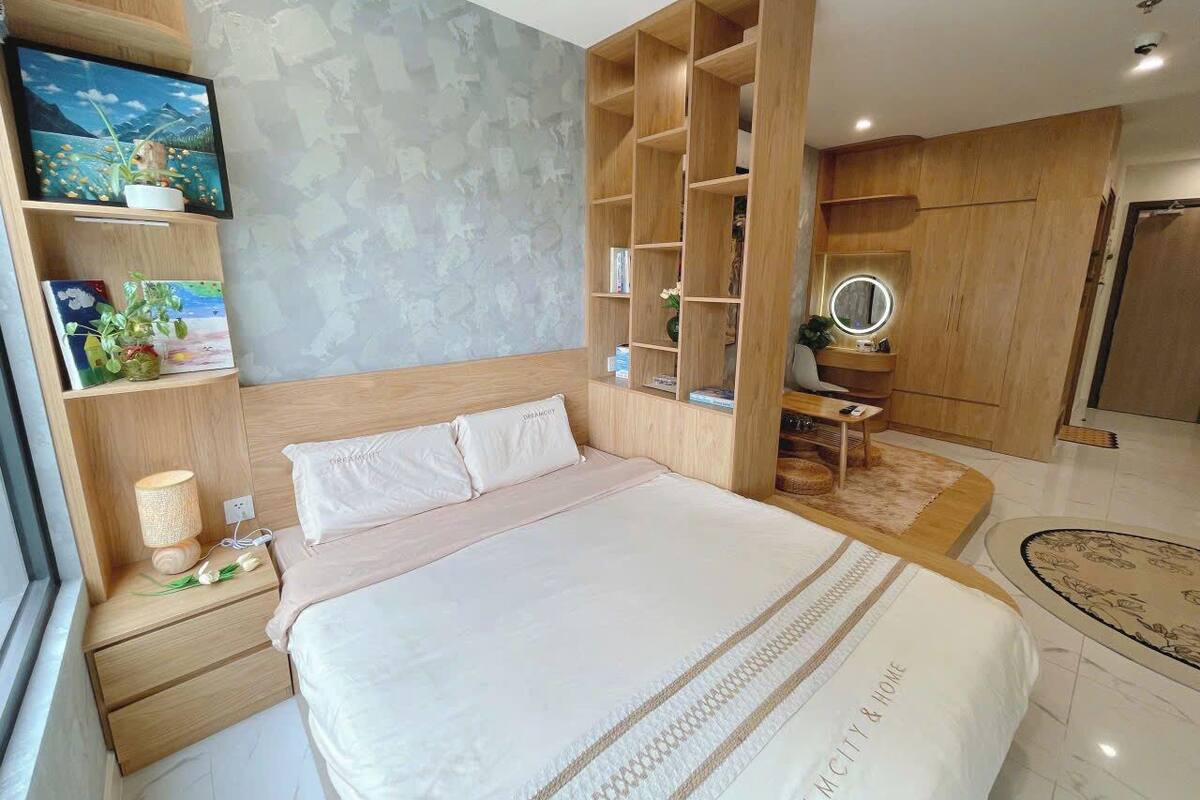A modern bedroom with a large bed, wooden headboard, built-in shelving, a bedside table with a lamp, and a small round mirror.
