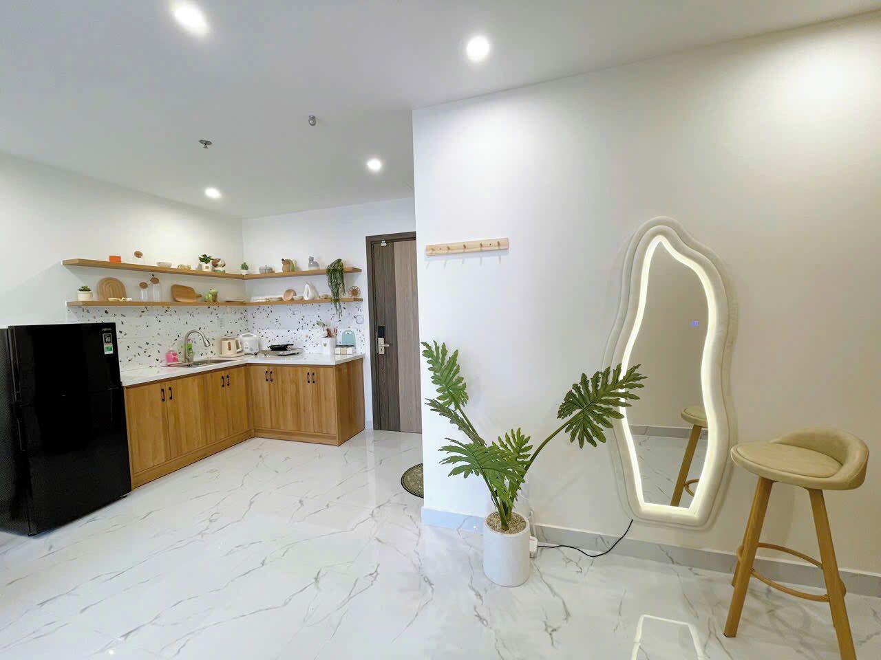 A modern kitchen with wooden cabinets, a black refrigerator, a marble floor, a potted plant, and a unique mirror.