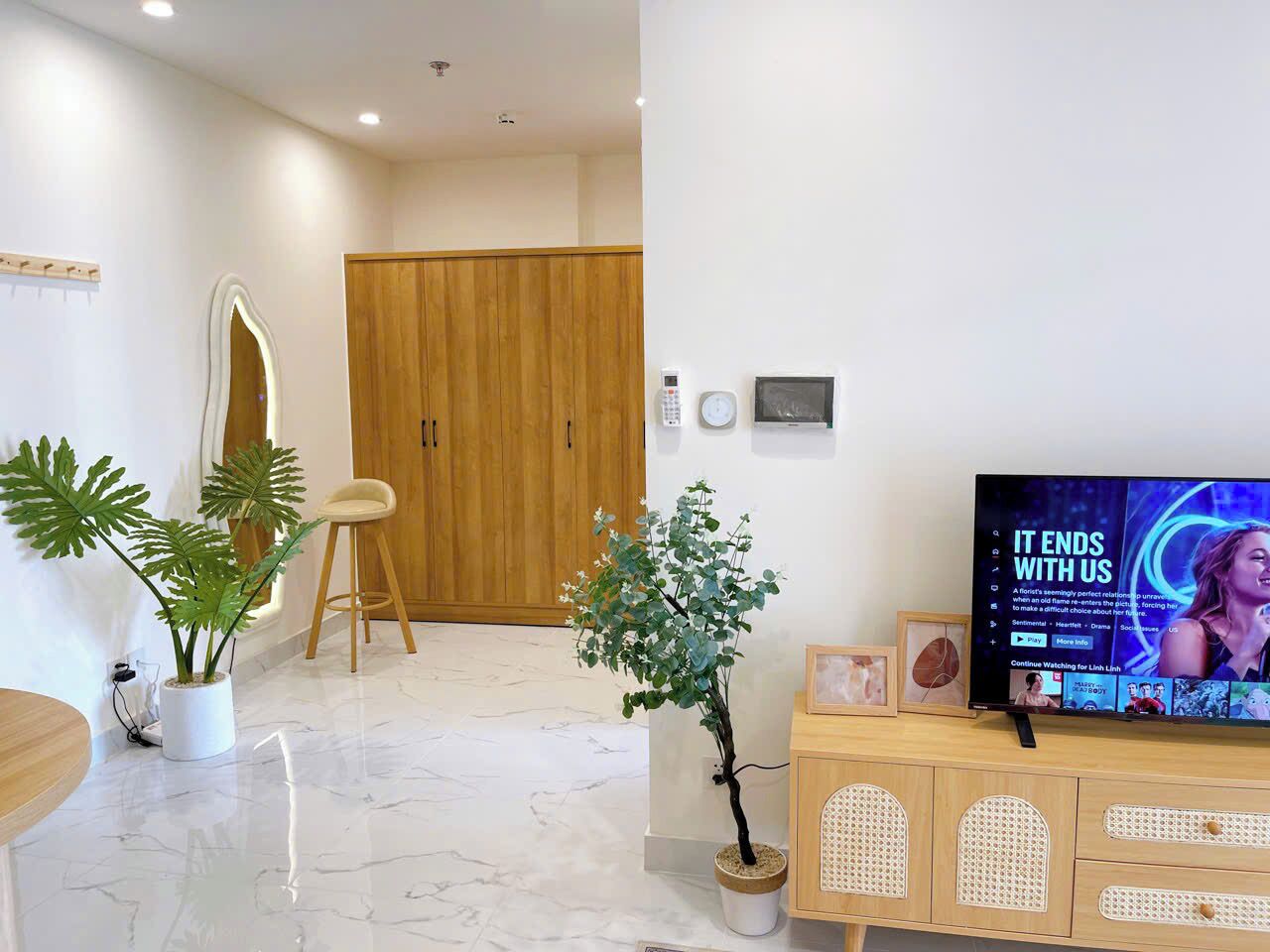 A modern living room with a flat-screen TV, wooden furniture, and potted plants.