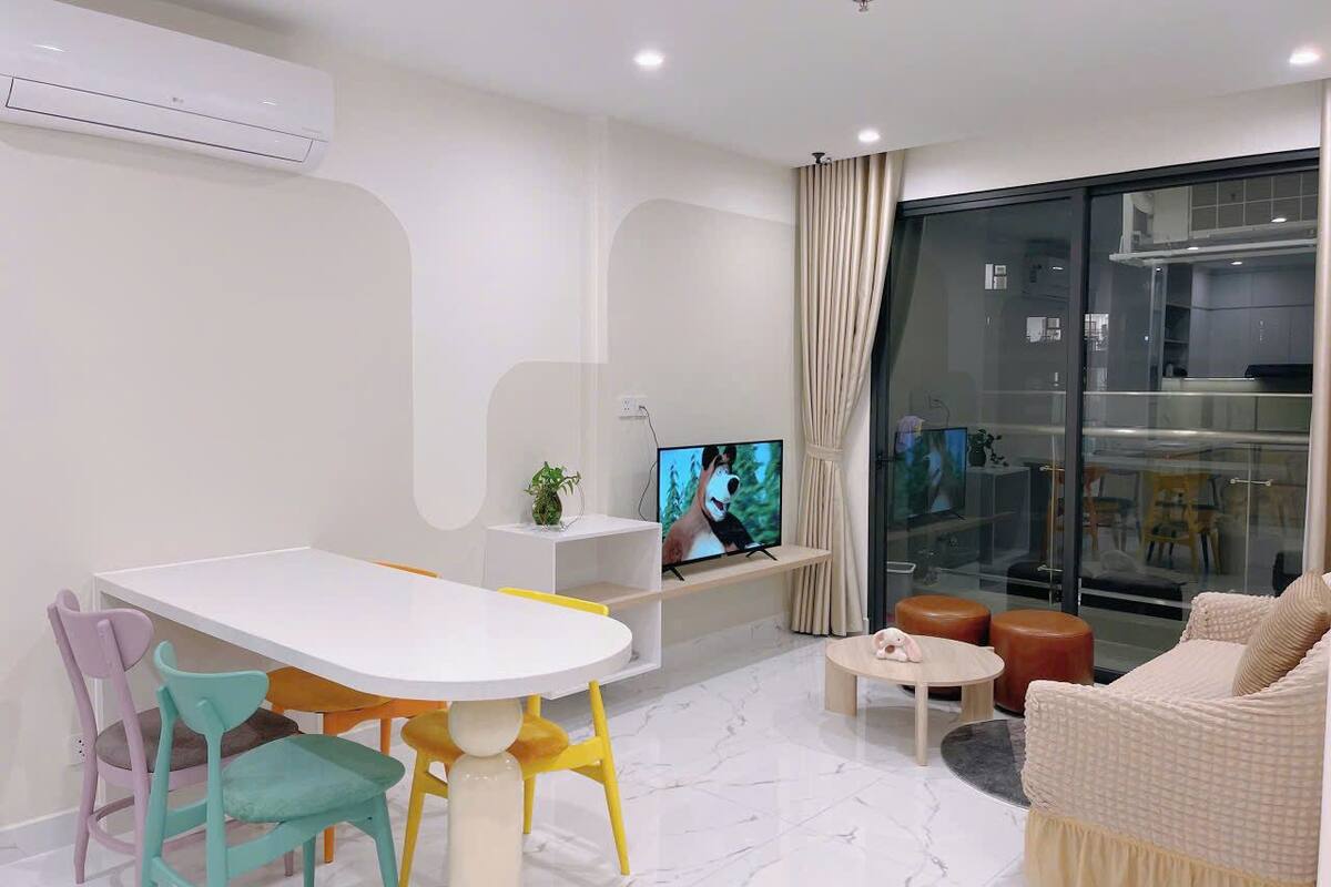 A modern living room with a white dining table, colorful chairs, a sofa, and a TV on a stand.