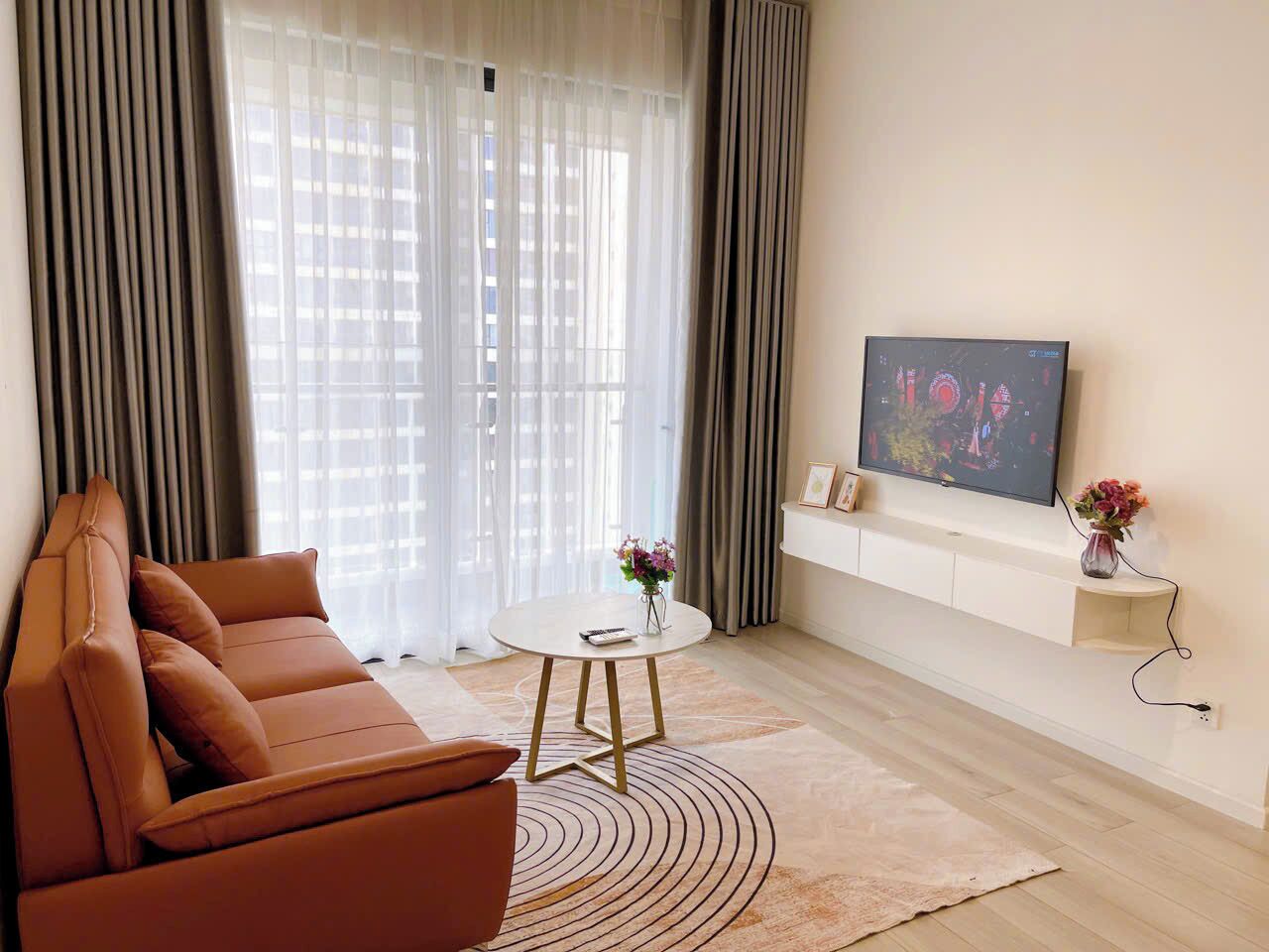 A modern living room with a brown leather sofa, a round coffee table, and a flat-screen TV mounted on the wall.