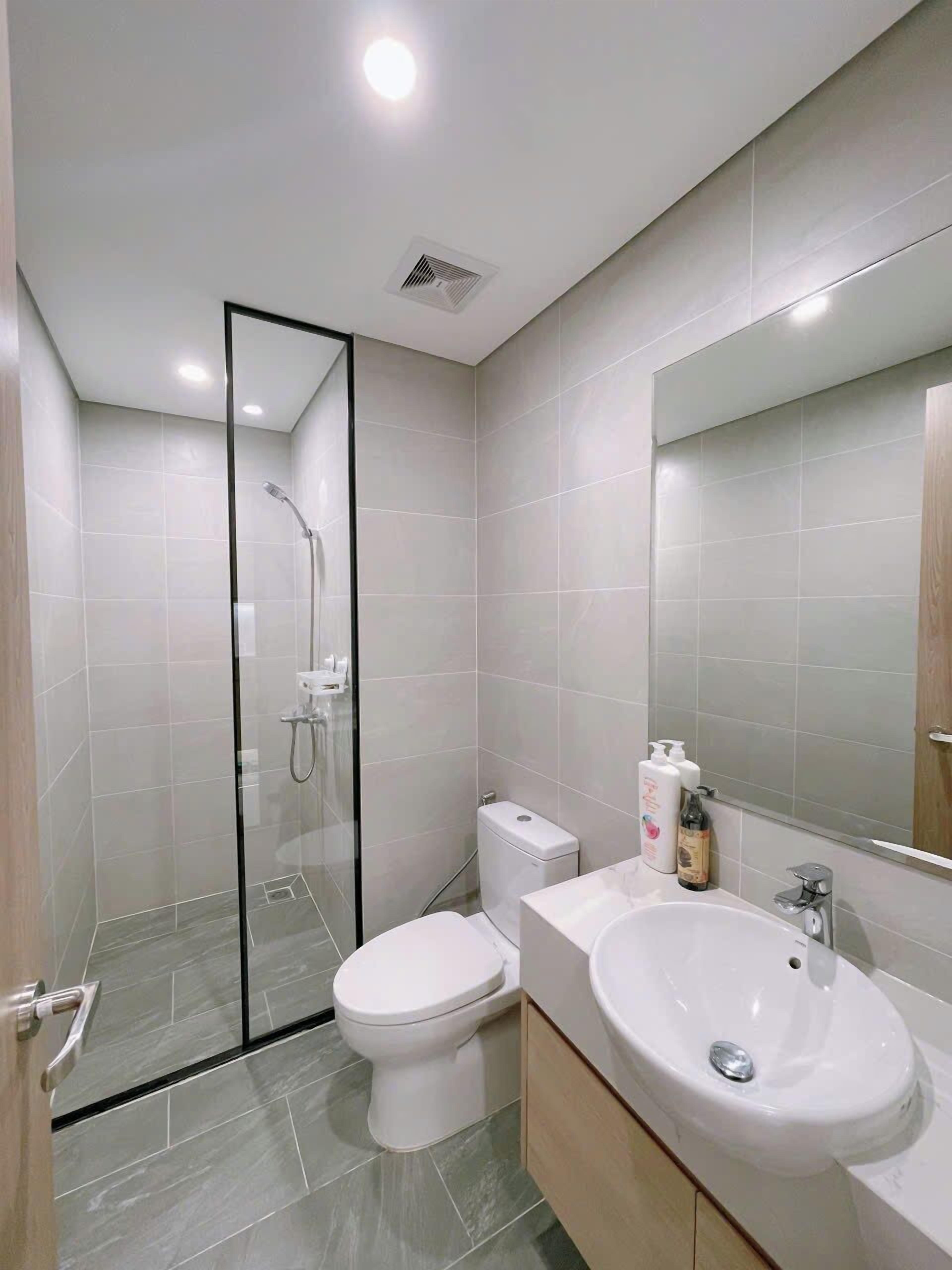 A modern bathroom with a glass-enclosed shower, a white toilet, and a sink with a mirror above it.
