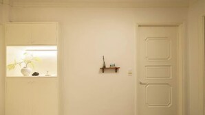 Una habitación con una puerta blanca, un estante pequeño con una planta y un armario con un jarrón.