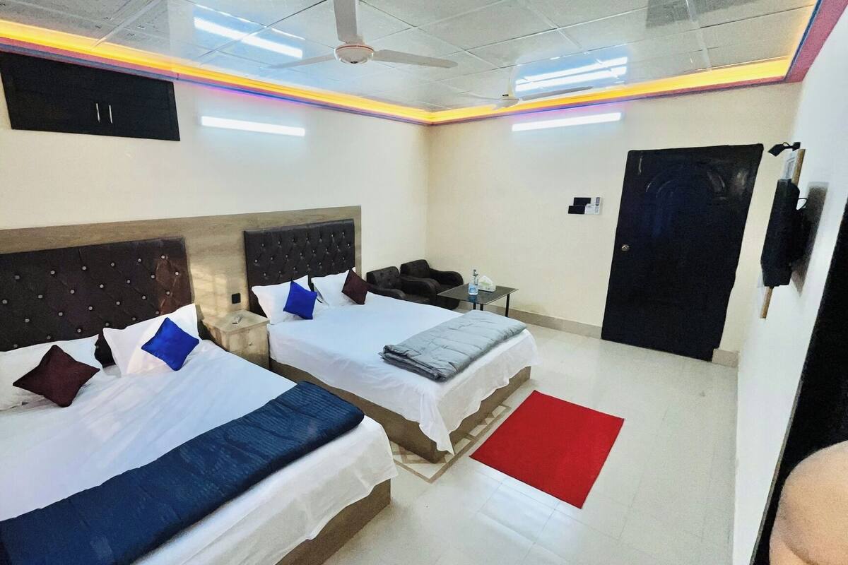 A hotel room with two beds, a red rug, a ceiling fan, and a door.