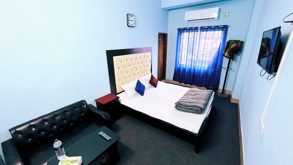Una habitación de hotel con una cama, un sofá de cuero negro, una mesita pequeña, un control remoto y un reloj en la pared.