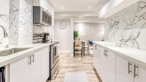 A modern kitchen with marble countertops, stainless steel appliances, and a wooden dining area. - The Cozy Cove on Flatford (Mississauga)