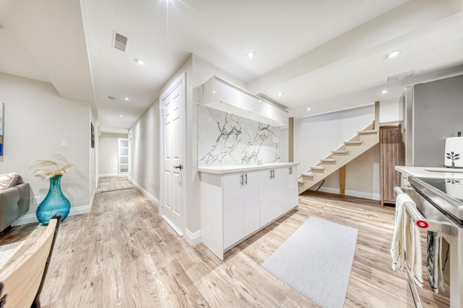 A modern kitchen with white cabinets, a marble backsplash, and a wooden staircase.