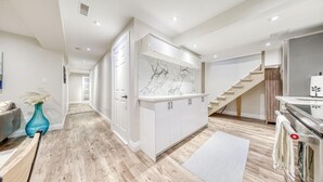 A modern kitchen with white cabinets, a marble backsplash, and a wooden staircase. - The Cozy Cove on Flatford (Mississauga)