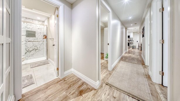 A hallway with wooden flooring, white walls, and a marble-tiled shower area. - The Cozy Cove on Flatford (Mississauga)