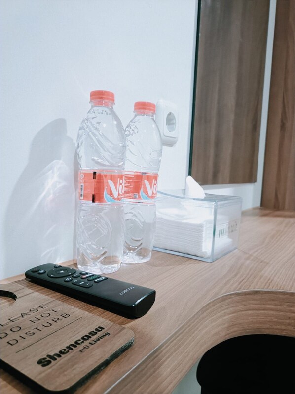 A wooden table with a remote control, two water bottles, a tissue box, and a small wooden sign. - Shencasa Living Juanda (Sidoarjo)