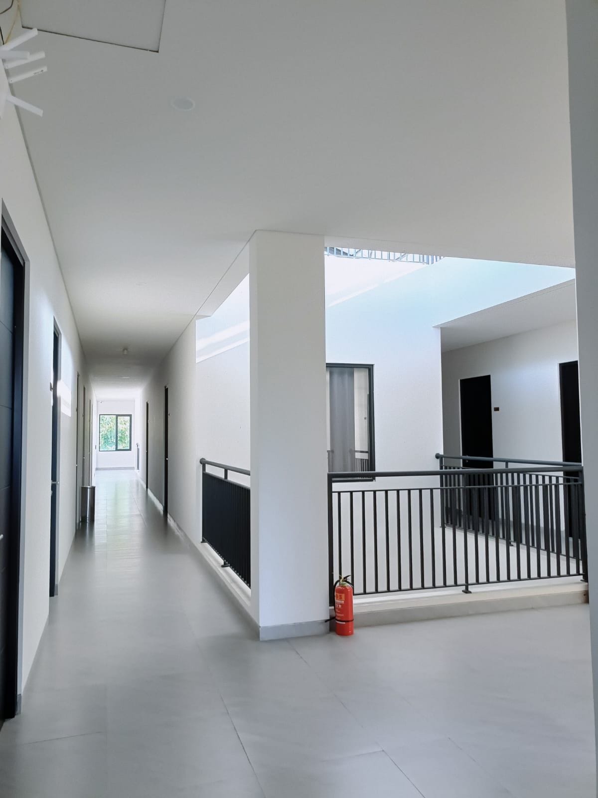 A corridor with a fire extinguisher, a balcony with a railing, and a door leading to another room.