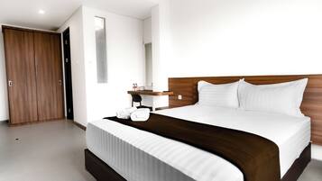 Habitación de hotel moderna con una cama grande, un armario de madera y una mesita de noche pequeña con lámpara.