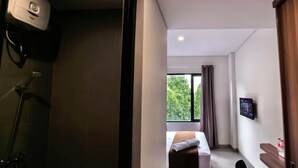 Ein modernes Hotelzimmer mit Dusche, einem Bett mit Handtuch, einem Fernseher an der Wand und einem Fenster mit Vorhängen.