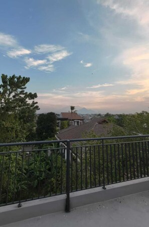 A balcony with a metal railing overlooking a residential area with houses and trees. - Shencasa Living Juanda (Sidoarjo)