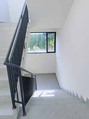 Un escalier avec une rampe métallique menant à un palier doté d’une fenêtre donnant sur un espace verdoyant.