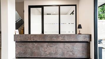 A reception desk with a glass partition, a staircase to the left, and a lamp on the right.