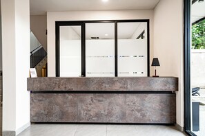 Un comptoir d’accueil avec une cloison en verre, un escalier sur la gauche et une lampe sur la droite.
