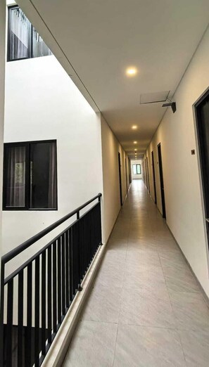 A long, narrow corridor with a tiled floor, black railings, and doors on both sides. - Shencasa Living Juanda (Sidoarjo)