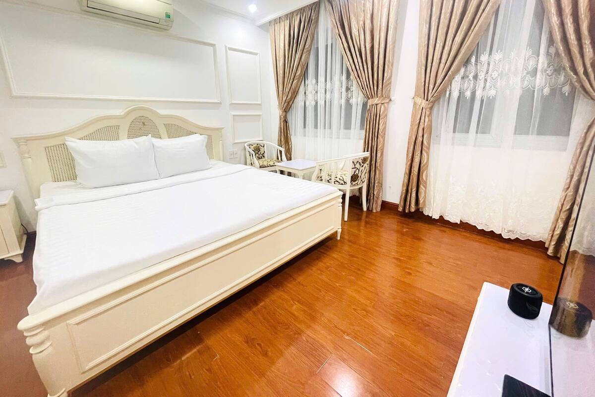 A hotel room with a large bed, a desk, a chair, and a window with curtains.