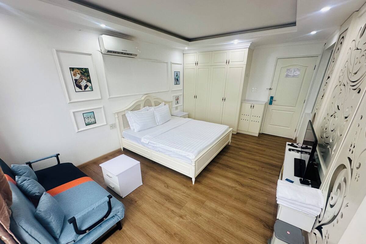 A bedroom with a bed, wardrobe, bedside table, and a desk with a chair.