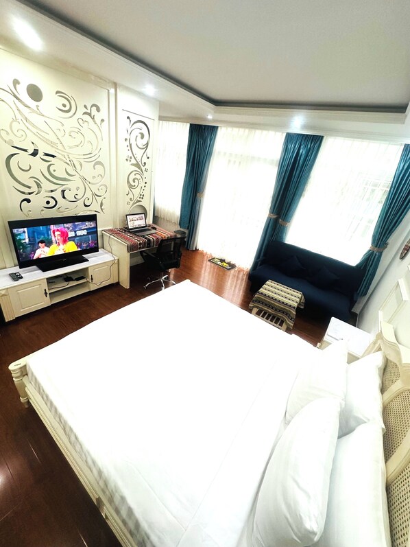 A hotel room with a large bed, a desk with a computer, a TV, and a window with curtains. - Diamond Suite Apartment (Ho Chi Minh City)