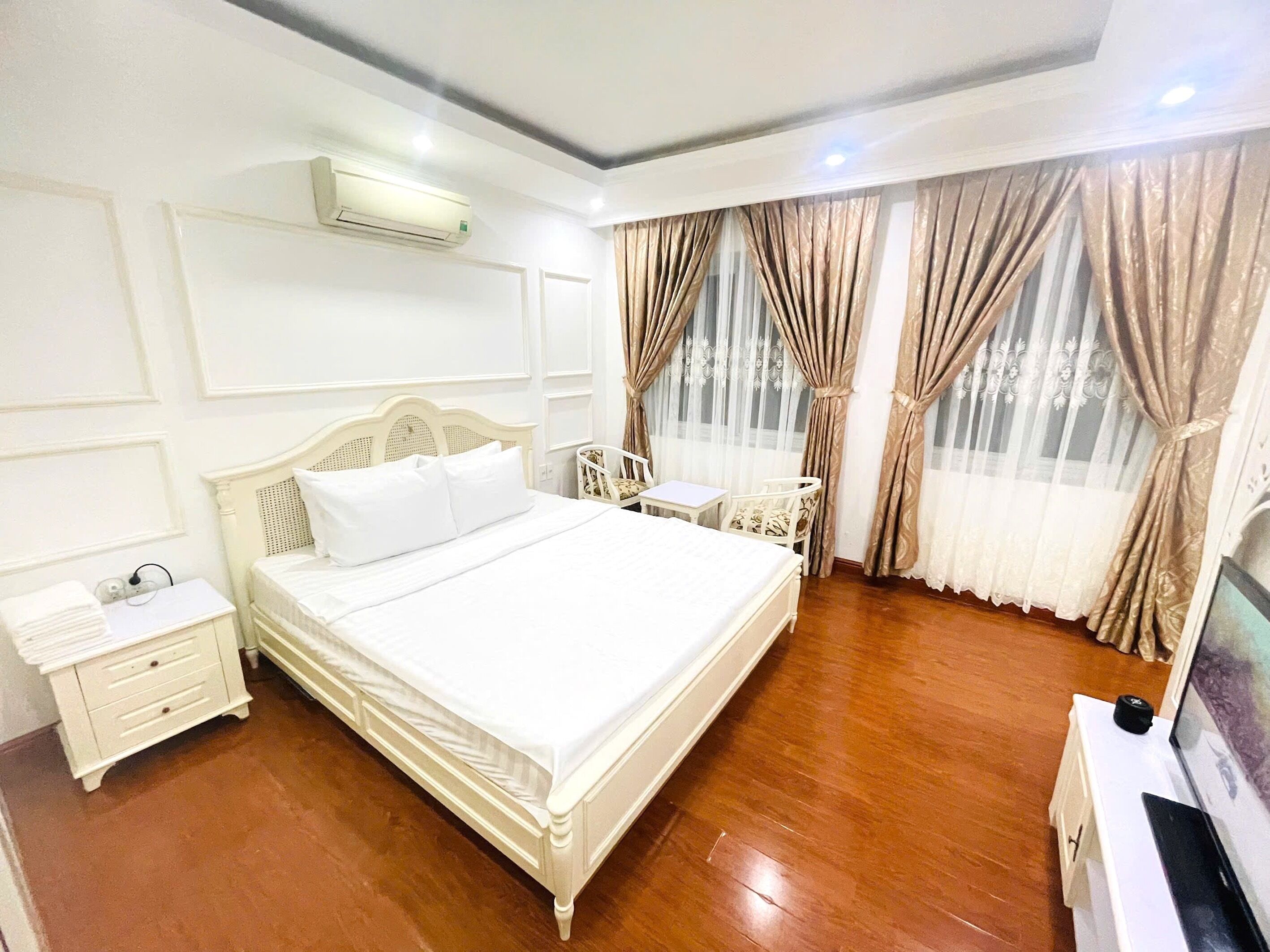 Un dormitorio ordenado con cama, mesitas de noche, una silla y un televisor.