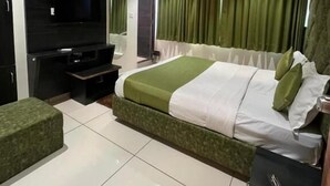 Ein modernes Schlafzimmer mit einem großen Bett, einem Flachbildfernseher, einem Deckenventilator und grünen Vorhängen.