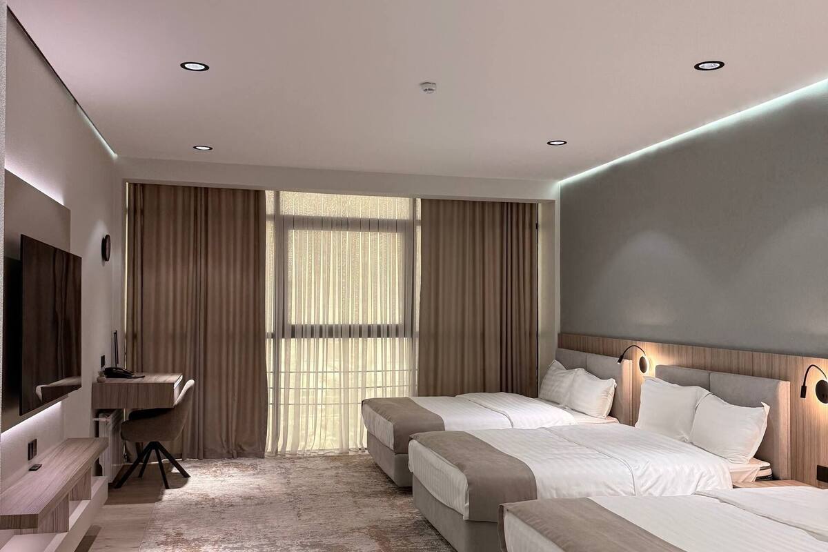 A modern hotel room with two beds, a desk, a TV, and a large window with curtains.