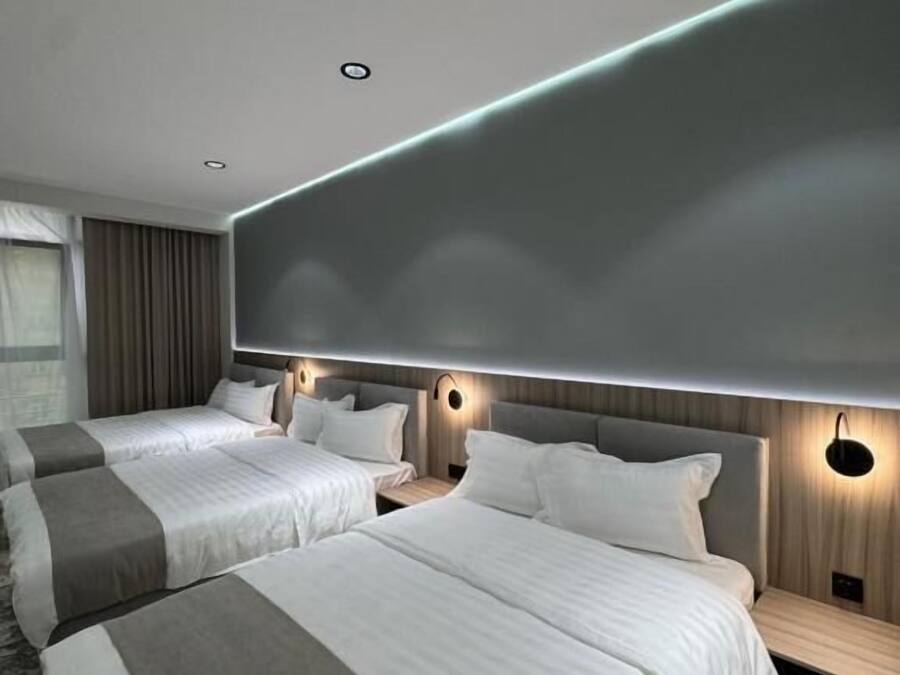 Una habitación de hotel moderna con dos camas, una lámpara grande en la pared y una ventana con cortinas.